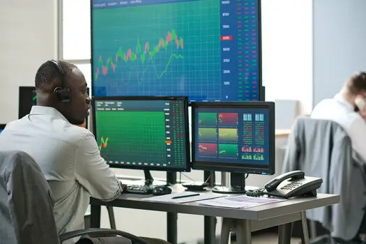 Broker wearing earphones while looking at charts on a computer and talking to a client