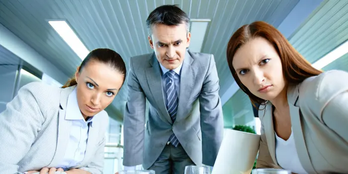 Photo of a man and two women in business suits, staring angrily back into the camera